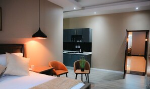 A modern hotel room with a bed, bedside table, and a small seating area with two chairs.