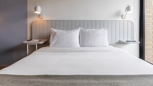 Ett modernt hotellrum med en stor säng, två sängbord och väggmonterade lampor.