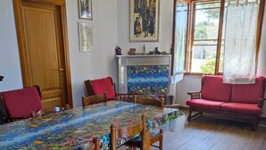 A dining room with a wooden table and chairs, a red sofa, and a fireplace with a colorful tiled surround. - Villa sul Mare (Sorso)