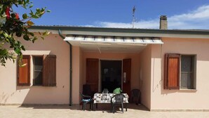 A building with a covered patio area, a table with chairs, and a window with shutters. - Villa sul Mare (Sorso)