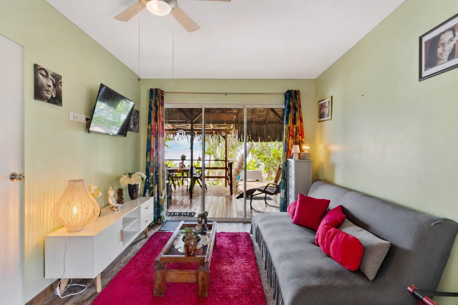 A room with a sofa, a television, a table with a lamp, and a view of the outdoors.