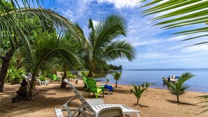 A beachside setting with a lounge chair, palm trees, and a small boat in the water. - Fare Oaoa · separate living room, beachfront, sleeps 4 (Moorea)