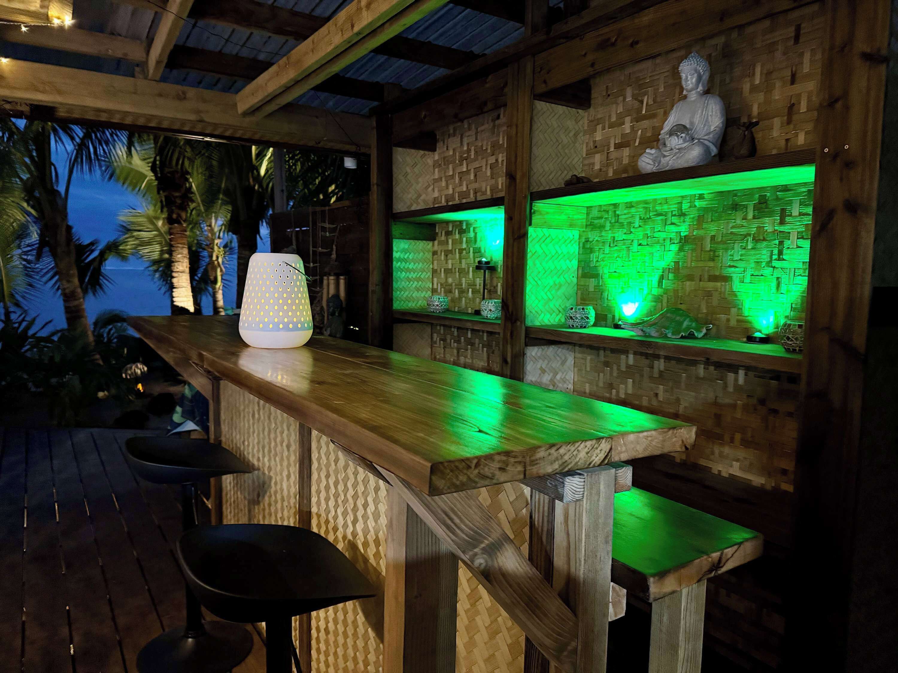 Un'area con bancone in legno, una statua di Buddha, illuminazione ambientale verde e un pannello decorativo in materiali tessili.