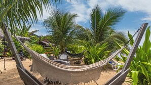 Een hangmat bevestigd aan een houten frame, met uitzicht op een tropische tuin en het strand.