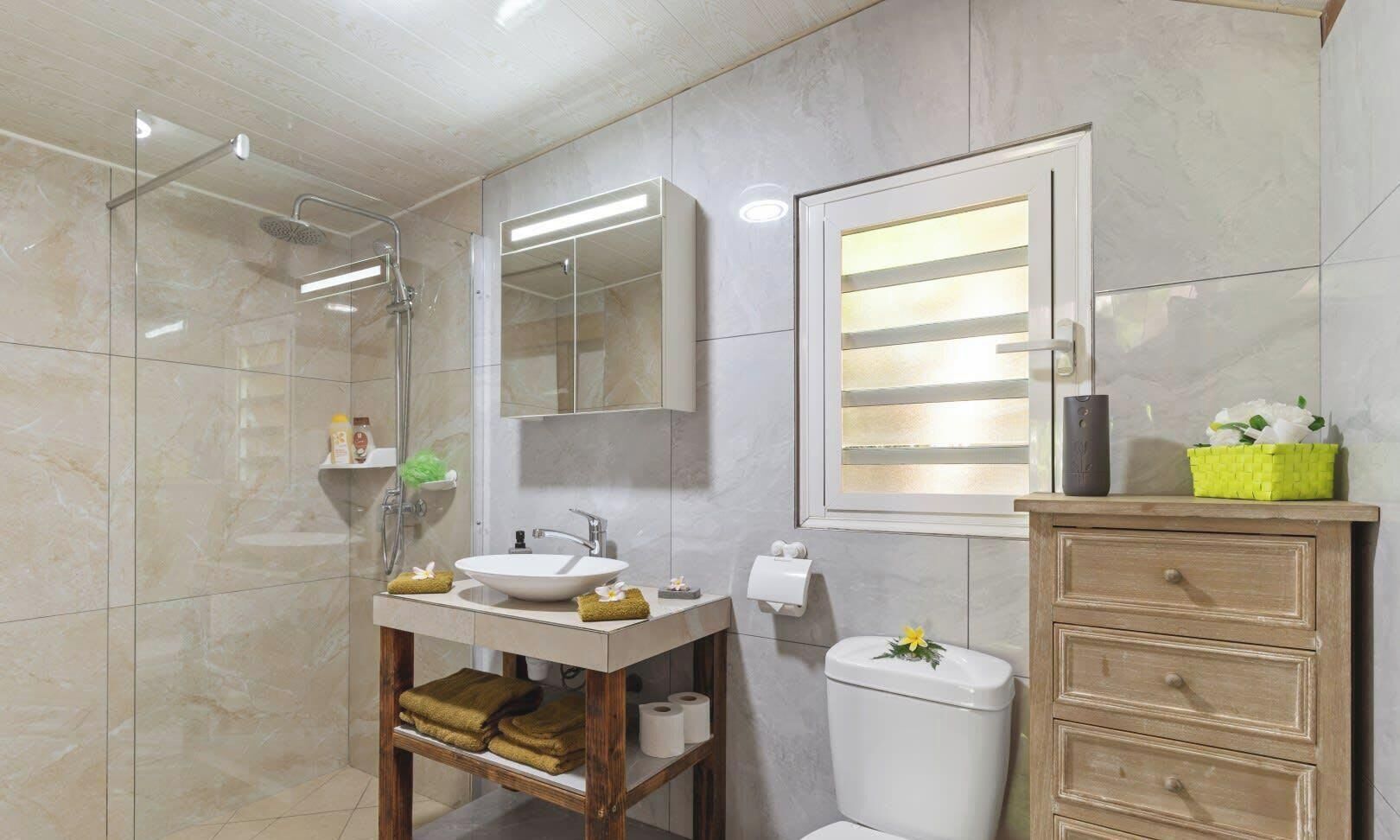 Une salle de bain moderne avec une douche à parois de verre, un meuble-lavabo avec un évier et un miroir, des toilettes et un meuble en bois avec des tiroirs.