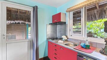 A compact kitchen with a red countertop, stainless steel sink, and a window with a view of greenery.