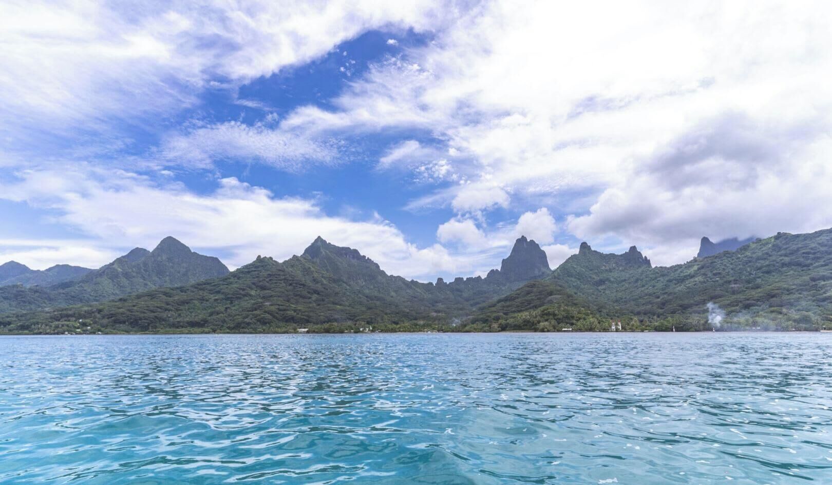 A coastal landscape with clear blue waters and mountainous terrain in the background.