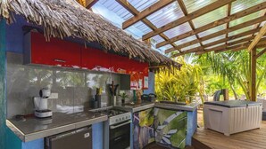 A compact kitchen with a gas stove, oven, and sink, a red cabinet, and a thatched roof. - Fare Oaoa · the quiet end of the beach, sleeps 2 (Moorea)