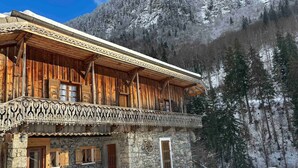 Una cabaña de madera con balcón, paredes de piedra y un paisaje cubierto de nieve.