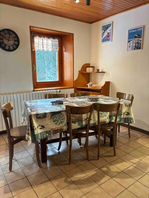 Un'area pranzo con un tavolo e sedie in legno, un orologio, una finestra con vista e due quadri appesi al muro.