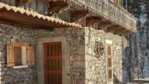 Un edificio de piedra con un balcón de madera, una puerta de madera y un pequeño banco.