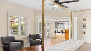 Ein modernes Schlafzimmer mit einem großen Bett, zwei Sesseln, einem Deckenventilator und einer Bar mit Hockern.