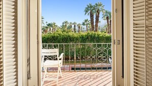 Ein Balkon mit weißem Stuhl, Metallgeländer und Blick auf Palmen und eine Hecke.