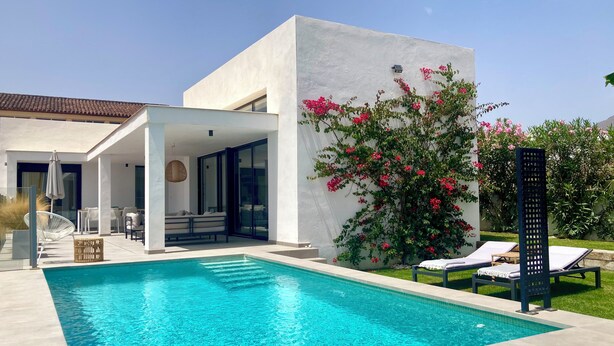 Una casa moderna amb piscina, mobiliari exterior i un jardí ple de flors roses.