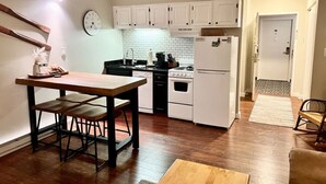 Une cuisine de taille réduite avec des meubles blancs, une table en bois et une horloge au mur.