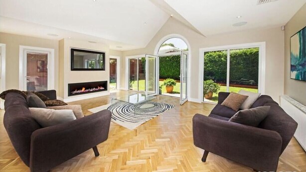 Ein großzügiges Wohnzimmer mit zwei Sofas, einem Kamin und großen Glasüren, die in einen Garten führen.