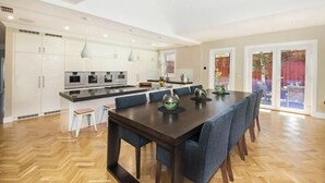 Eine moderne Küche mit weißen Schränken, einer zentralen Kochinsel und einem Essbereich mit einem dunklen Holztisch und blauen Stühlen.