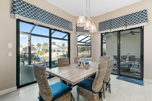 Un comedor con mesa de madera, sillas de mimbre y vistas a través de puertas de cristal amplias.
