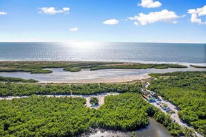 Vue aérienne d’une zone côtière avec des forêts de mangroves, une plage de sable et un espace de stationnement.