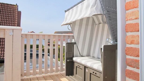 A balcony with a wooden fence, a cushioned seating area, and a view of the street. - Möwenstraße 9 Haus 3 Inkl. Wlan (Grömitz)