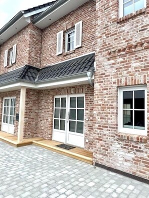 Un bâtiment à deux étages, construit en briques, avec un toit recouvert de tuiles, des fenêtres à cadre blanc et une entrée abritée.