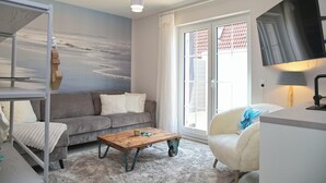 A modern living room with a grey sofa, a wooden coffee table, a white armchair, and a large window with a view of the beach. - Möwenstraße 9 Haus 3 Inkl. Wlan (Grömitz)