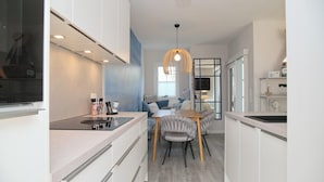 A modern kitchen with white cabinetry, a dining area with a wooden table and chairs, and a hanging pendant light. - Möwenstraße 9 Haus 3 Inkl. Wlan (Grömitz)