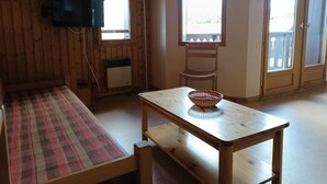A cozy room with a wooden floor, a plaid rug, a wooden table with a basket, a television mounted on the wall, and a window with a view of greenery. - Apartment for 4, near slopes and shops, Crest-Voland (Crest-Voland)