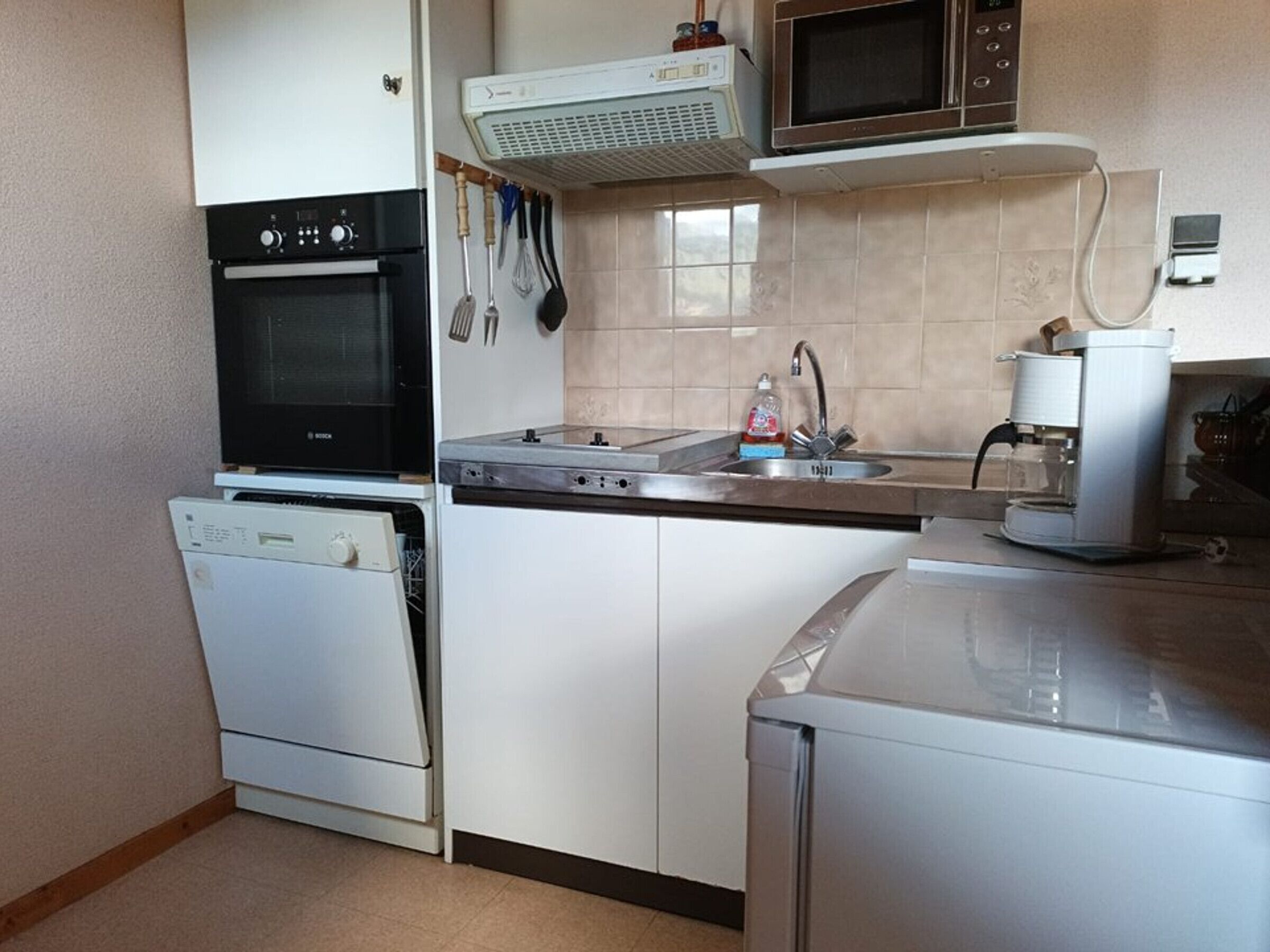 A compact kitchen with a dishwasher, oven, microwave, and coffee maker.