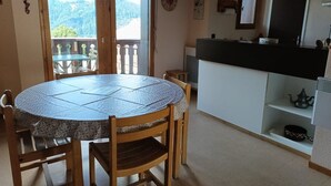 A dining area with a round table, wooden chairs, a kitchen counter, and a view of a balcony with a table and chairs outside. - Apartment for 4, near slopes and shops, Crest-Voland (Crest-Voland)