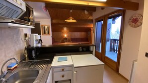 A compact kitchen with a sink, a coffee machine, and a small refrigerator. There is a wooden ceiling with exposed beams and a hanging light fixture. A window provides a view of the outside. - Apartment for 4, near slopes and shops, Crest-Voland (Crest-Voland)