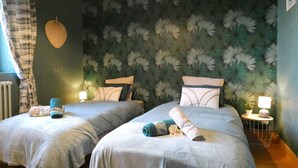 Habitación de hotel con dos camas, un cabecero de gran tamaño con estampado floral y una pequeña mesa con lámpara.