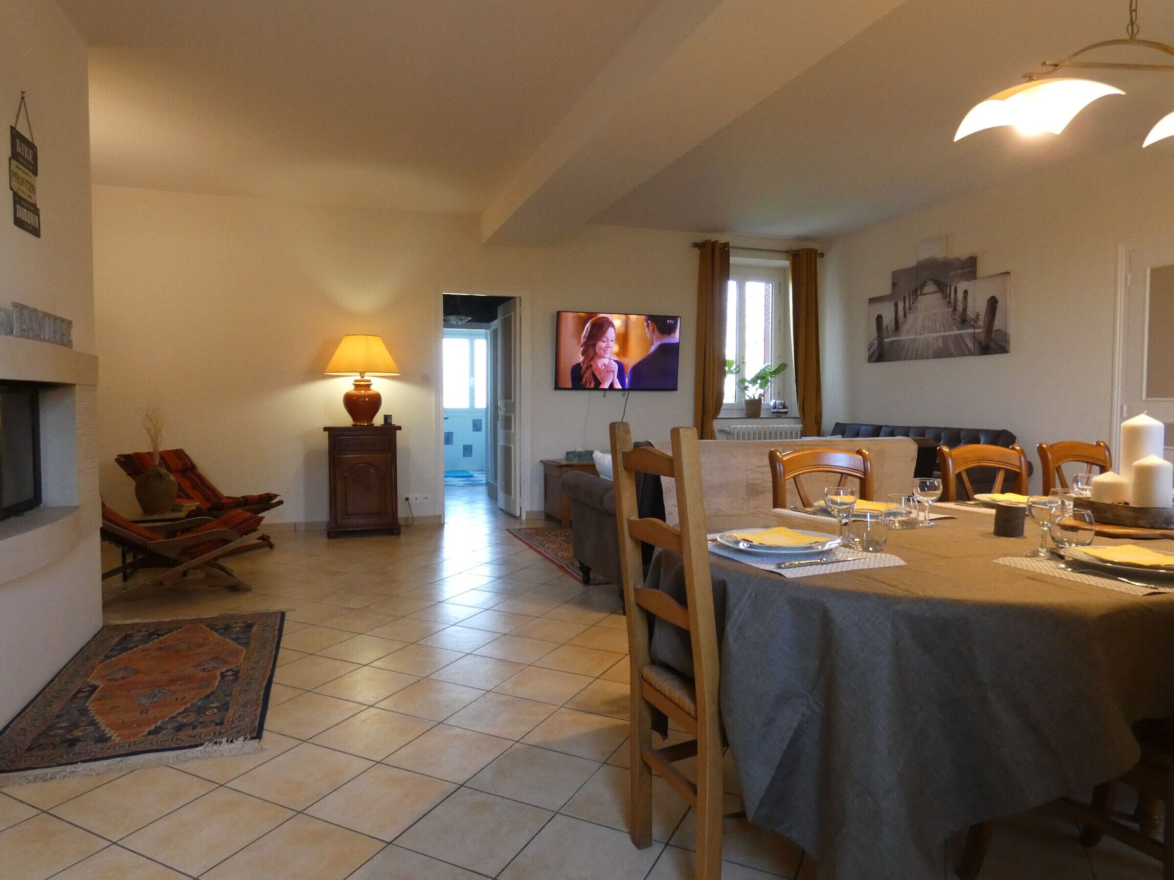 A dining area with a table set for four, a television mounted on the wall, and a fireplace with a lamp.