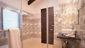 Un baño moderno con cabina de ducha de vidrio, un lavabo blanco y una zona de ducha con azulejos de mármol.
