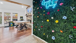Une pièce avec un mur vert décoré de fleurs colorées, un néon affichant le message « Seules les bonnes ondes » et une table de billard.