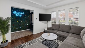 Un salon moderne avec un canapé d’angle gris, une table basse ronde et un téléviseur à écran plat fixé au mur.