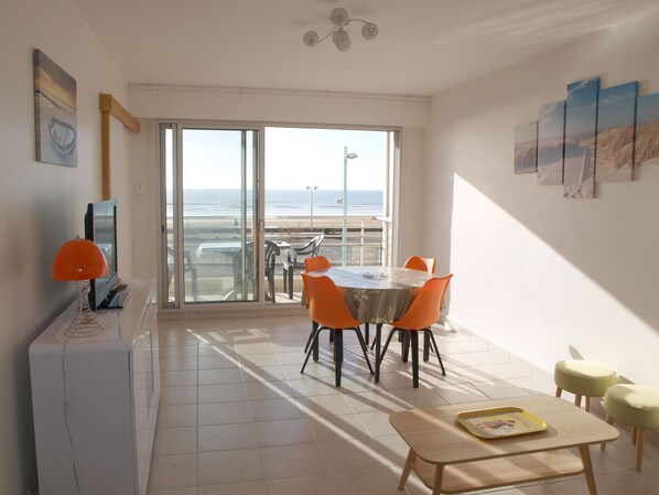 A modern living room with a large sliding glass door leading to a balcony with a view of the beach.