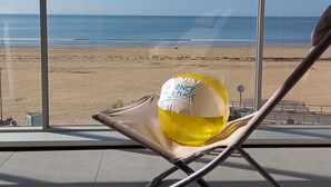 A beach view from a room with large windows, featuring a beach ball and a chair.