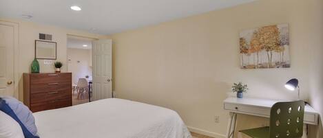 A bedroom with a bed, dresser, desk, chair, and a painting on the wall.