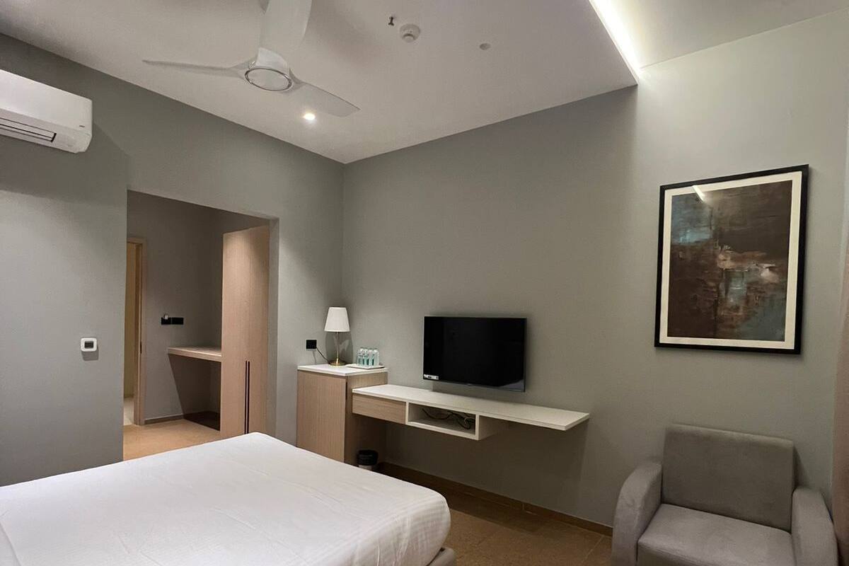 A hotel room with a bed, a TV, a chair, a desk with a lamp, and a painting on the wall.