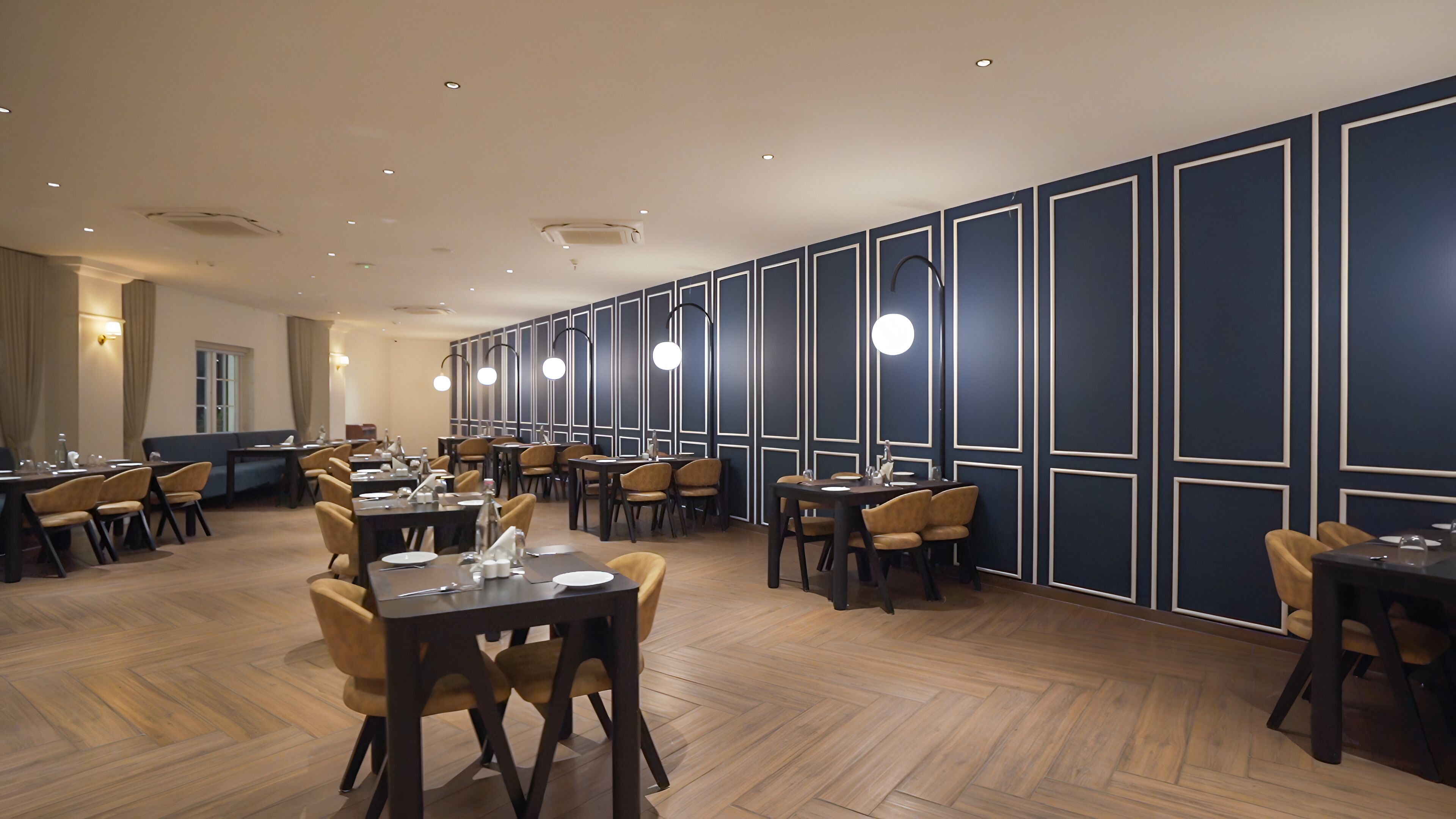 A spacious dining area with multiple tables and chairs, a long counter, and a wall with geometric paneling.