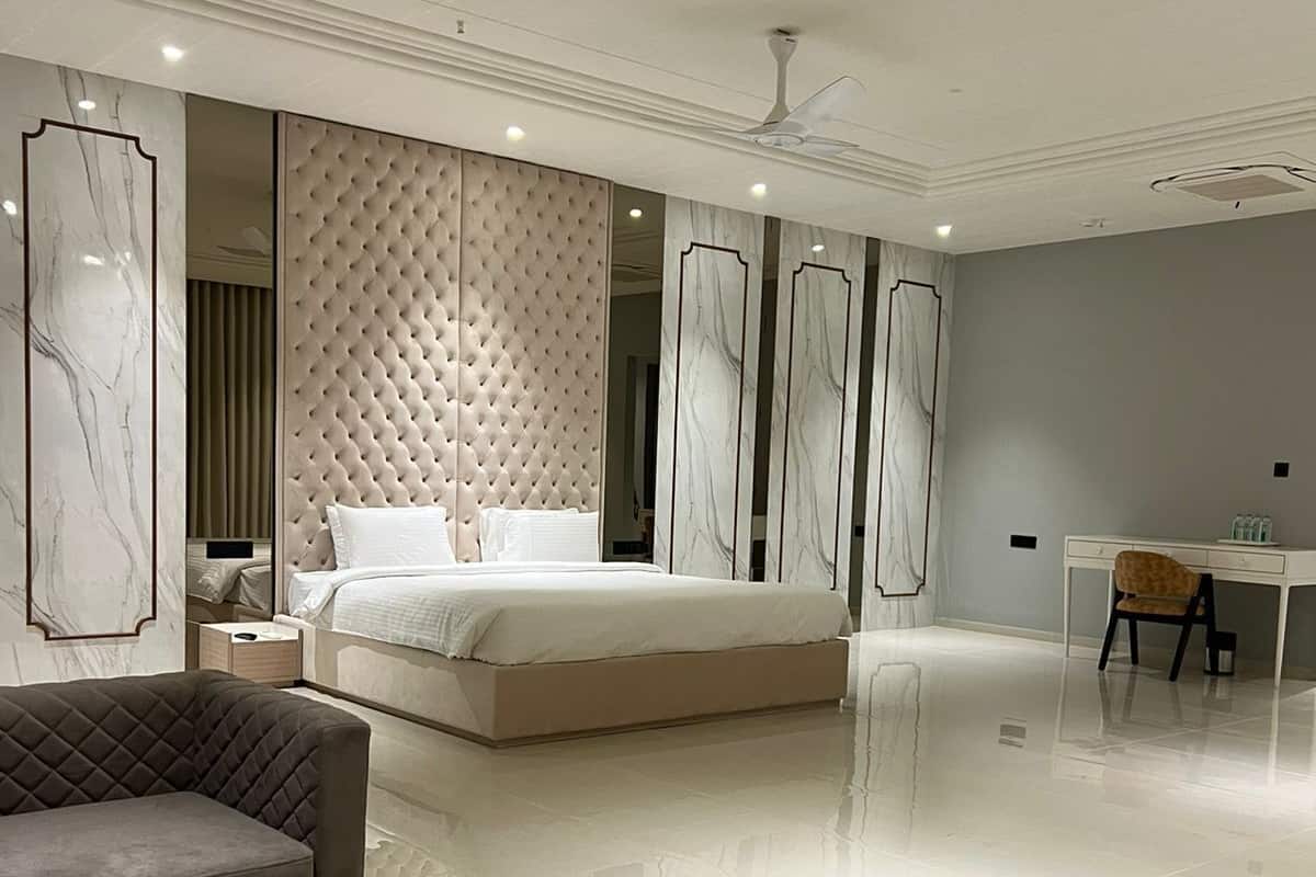 A modern bedroom with a large bed, a sitting area with a sofa and a coffee table, and a desk with a chair.