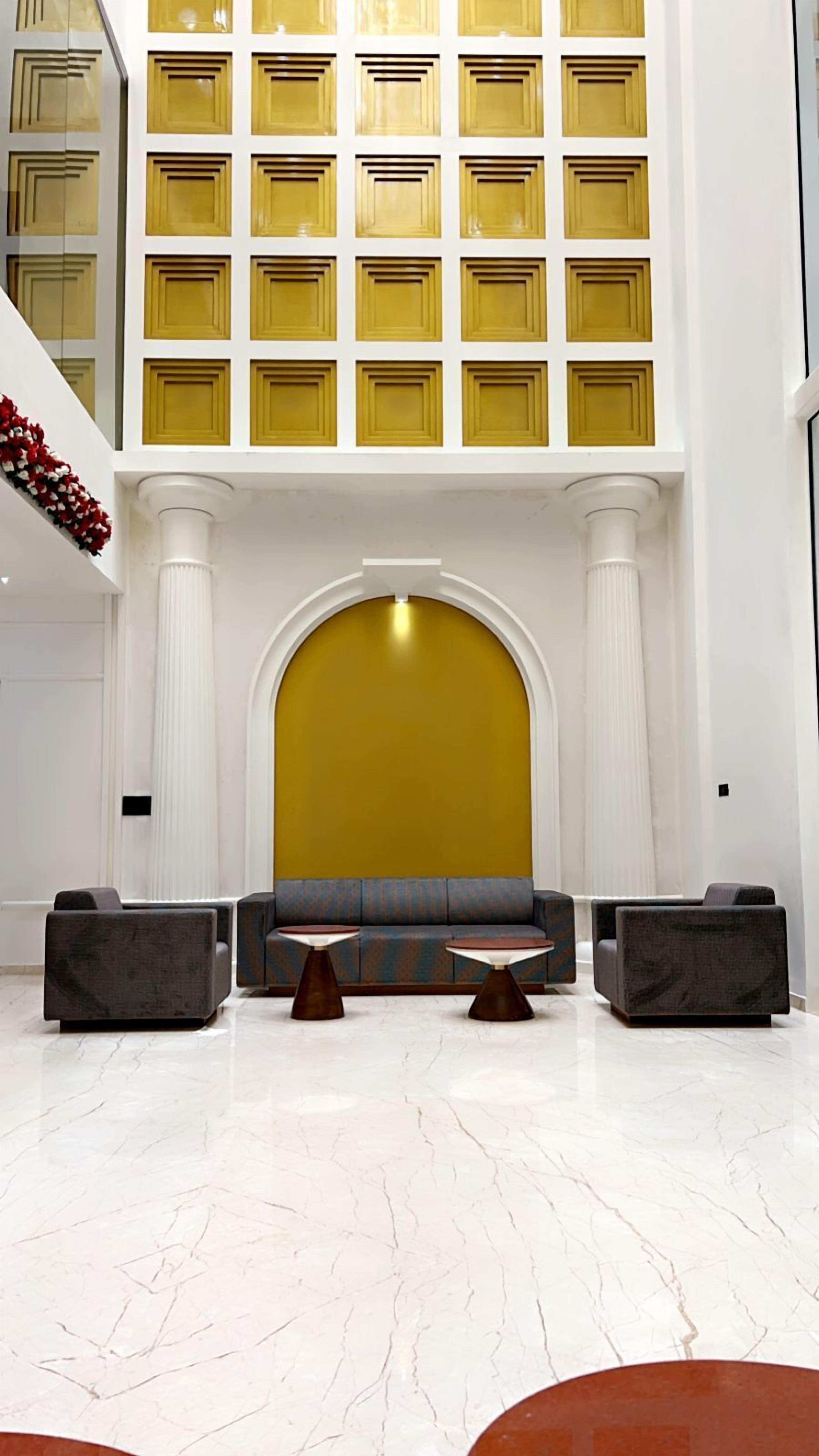 Un hall d’entrée spacieux avec un plafond haut, une grande fenêtre en arc de cercle et un coin salon avec des canapés et des tables.