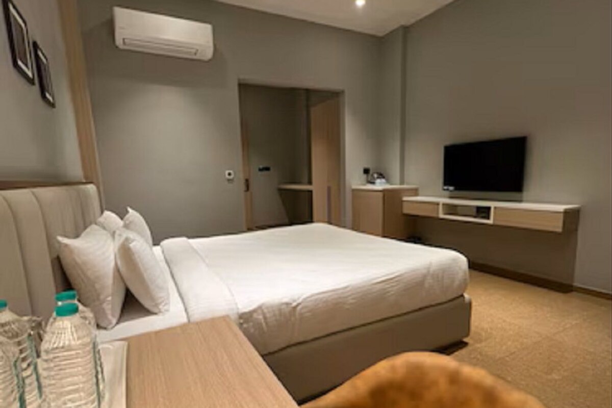 A hotel room with a bed, a desk with water bottles, a TV, and a ceiling fan.