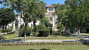 A large, historic building with a symmetrical facade, surrounded by well-maintained gardens and trees.