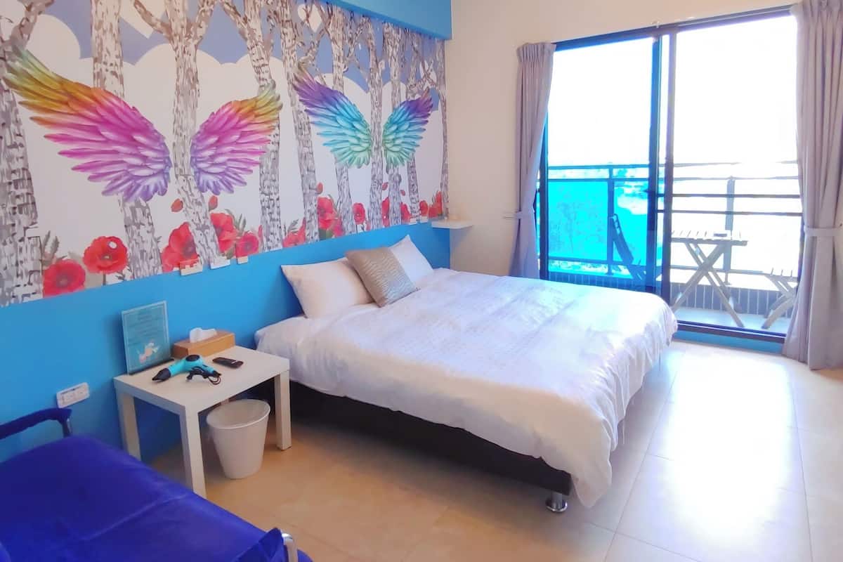 A bedroom with a bed, a desk, a chair, and a balcony with a view.