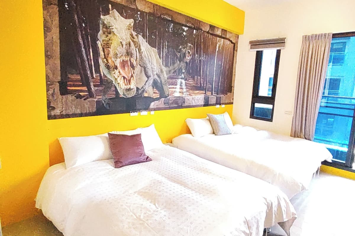 A hotel room with two beds, a large painting on the wall, and a window with curtains.