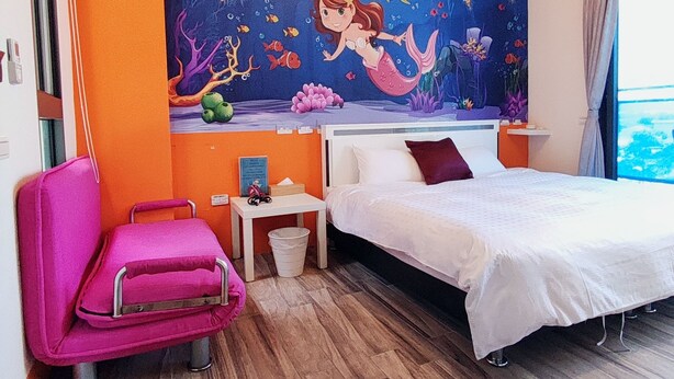 Une chambre d’hôtel avec un lit, une chaise, une table de chevet et une fresque représentant une sirène.