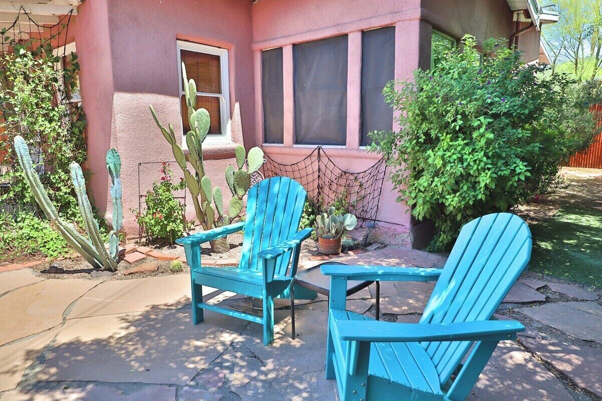 A patio with two blue Adirondack chairs, a cactus, and a potted plant.