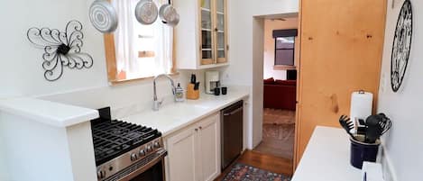 Une cuisine équipée d’une cuisinière à gaz, de meubles blancs, d’un évier et d’un tapis à motifs.